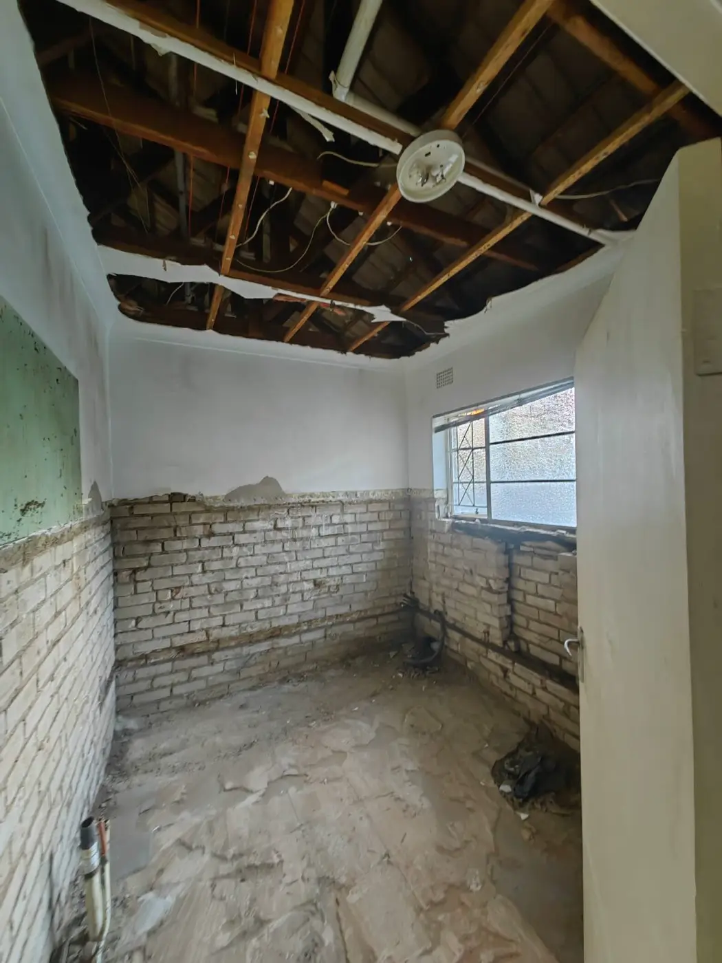 Old bathroom stripped back to bare brick, with the ceiling open