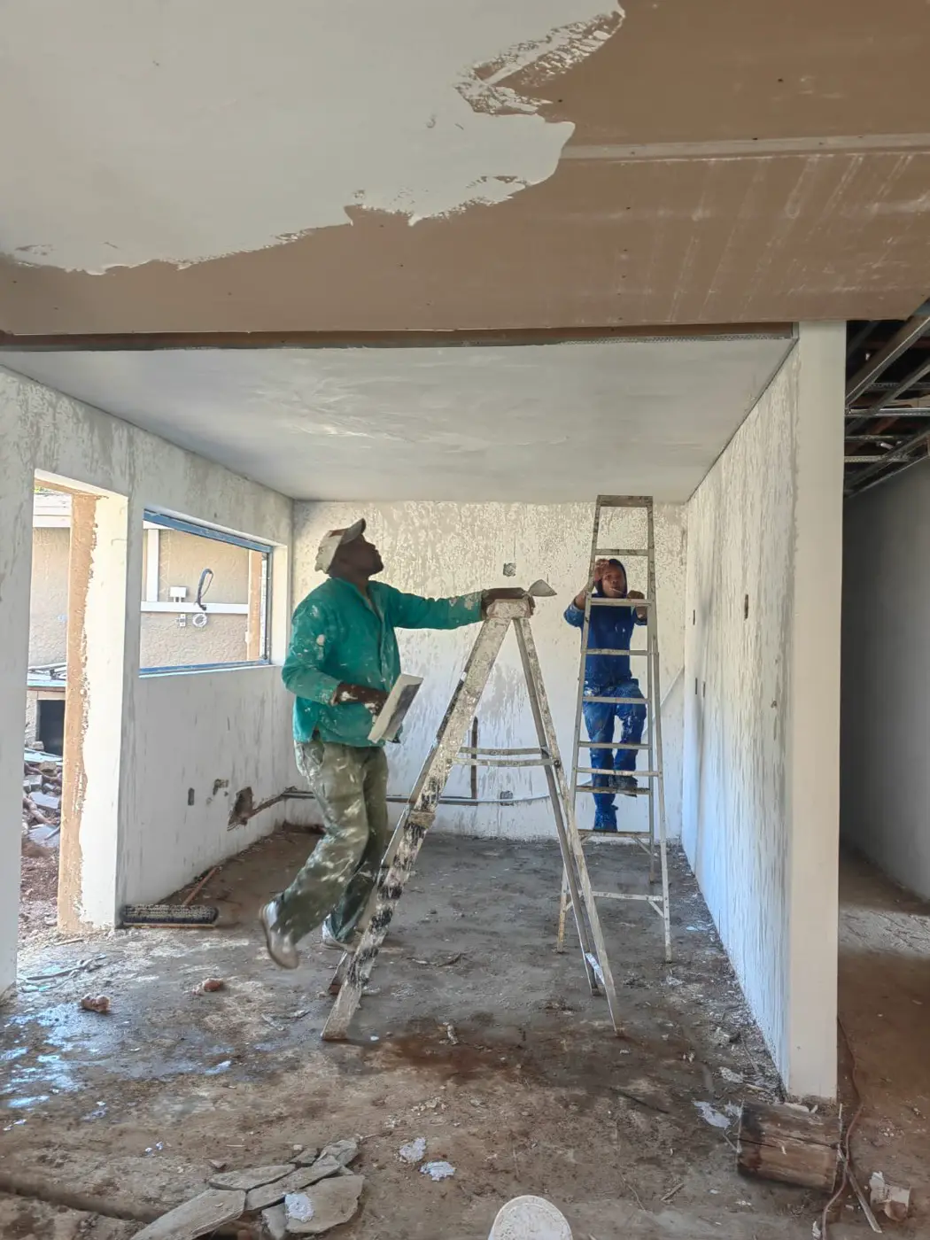 Plasterers on a ladder working on a long open-plan room