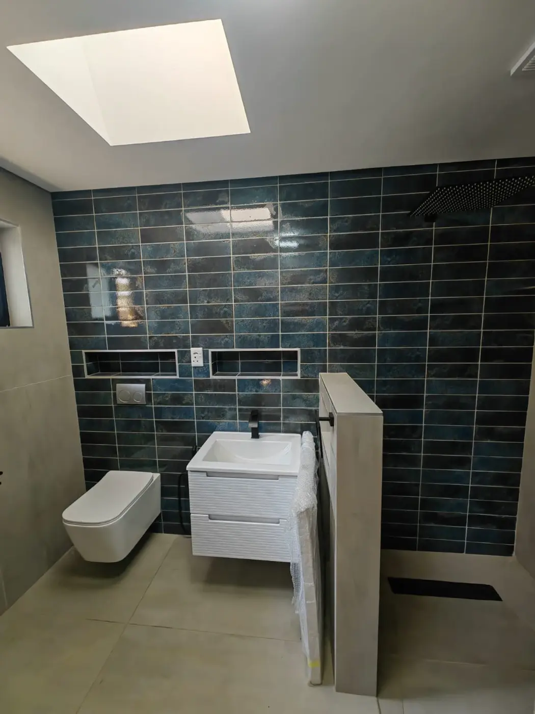 Finished bathroom with deep blue gloss wall tiles, a floating basin and a wall-hung toilet