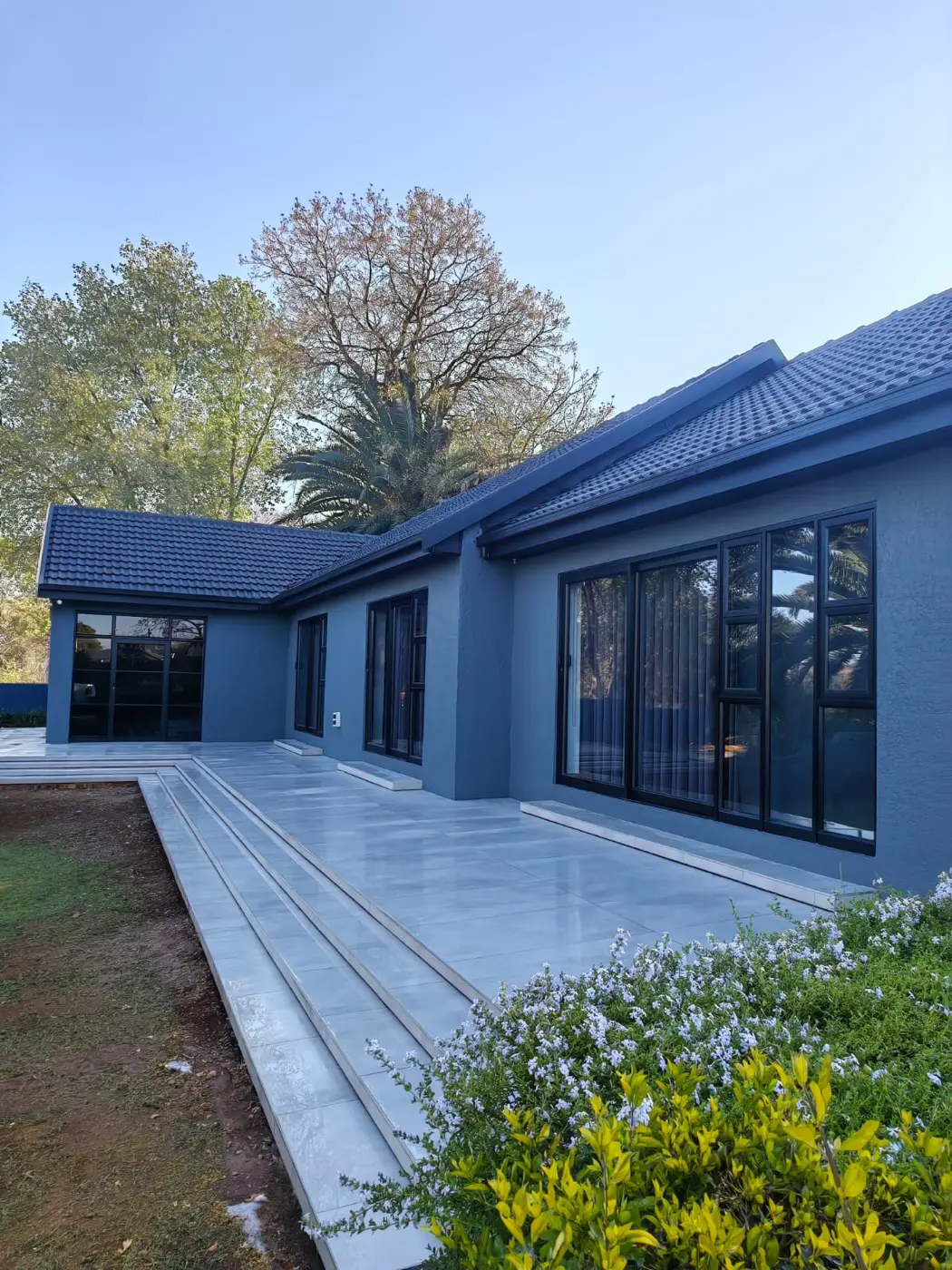 Renovated single-storey home painted dark blue with black-framed glass doors and a new concrete patio