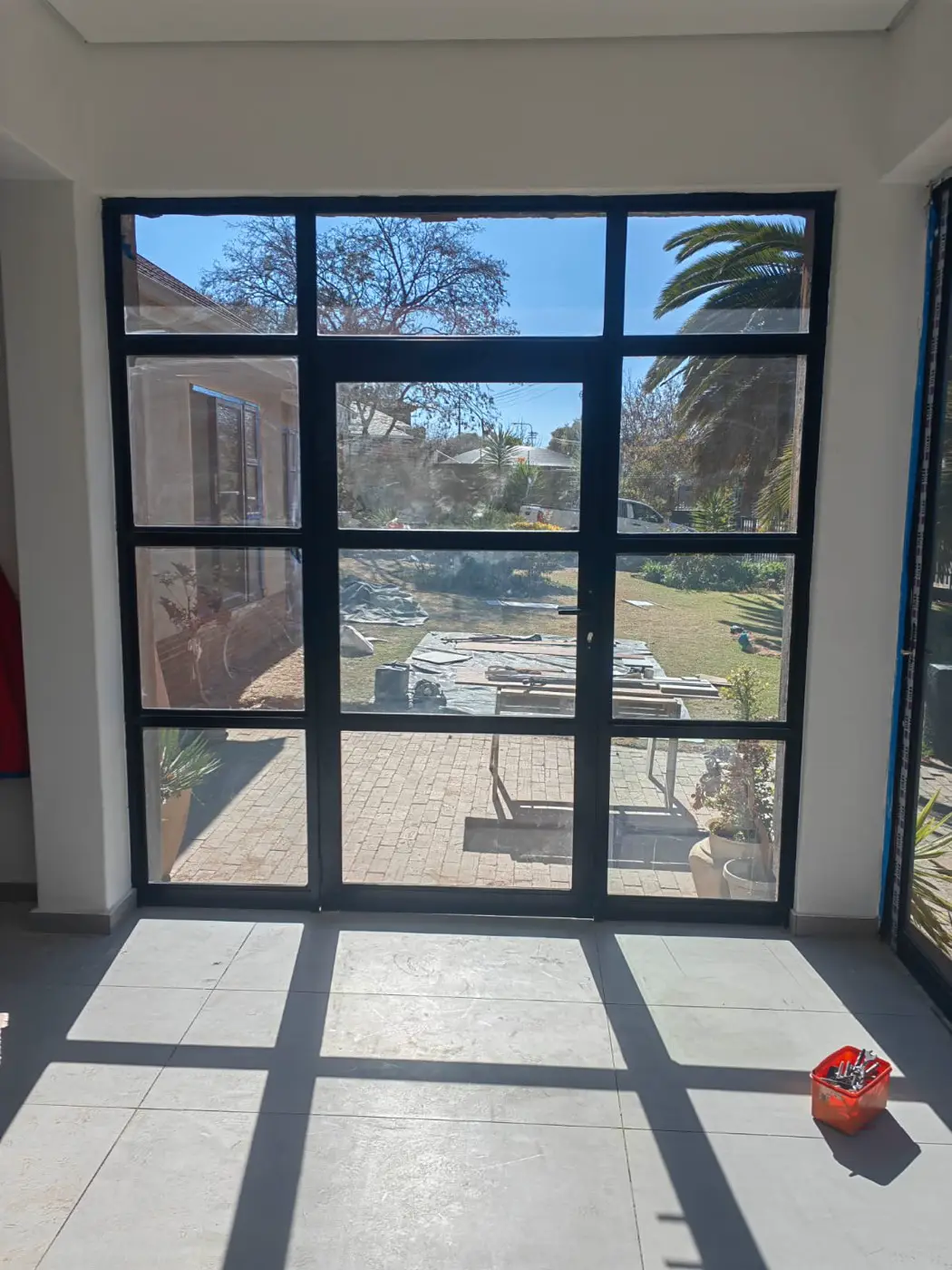 Black steel-framed glass door from inside, with sunlight across the tiles