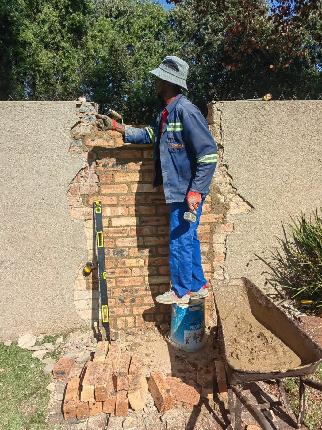 A builder rebuilding a broken-out section of the boundary wall in brick